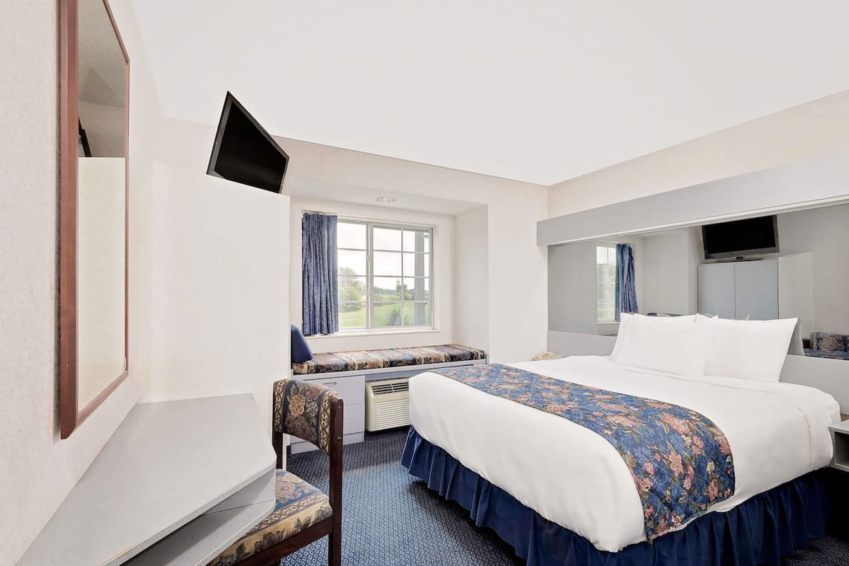 Habitación de hotel con una cama grande, un escritorio con silla, un televisor y una ventana con cortinas.