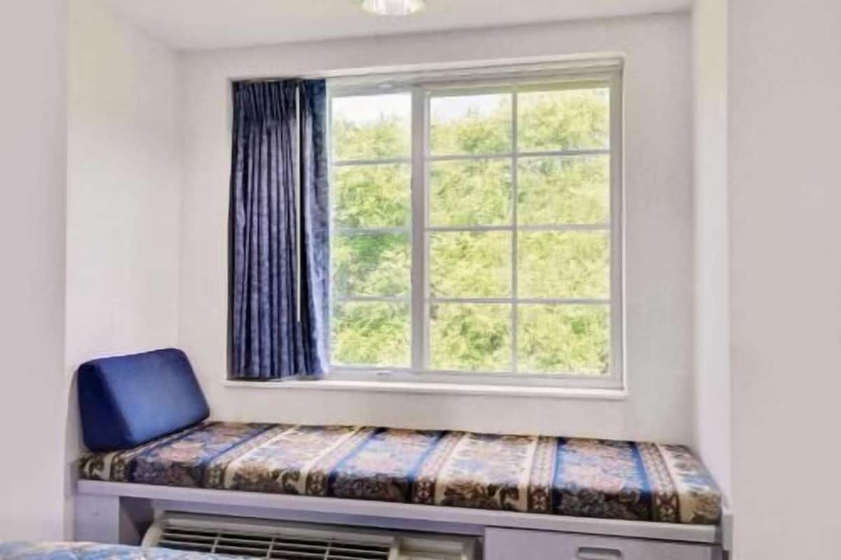 Una habitación pequeña con ventana, un banco y un radiador.