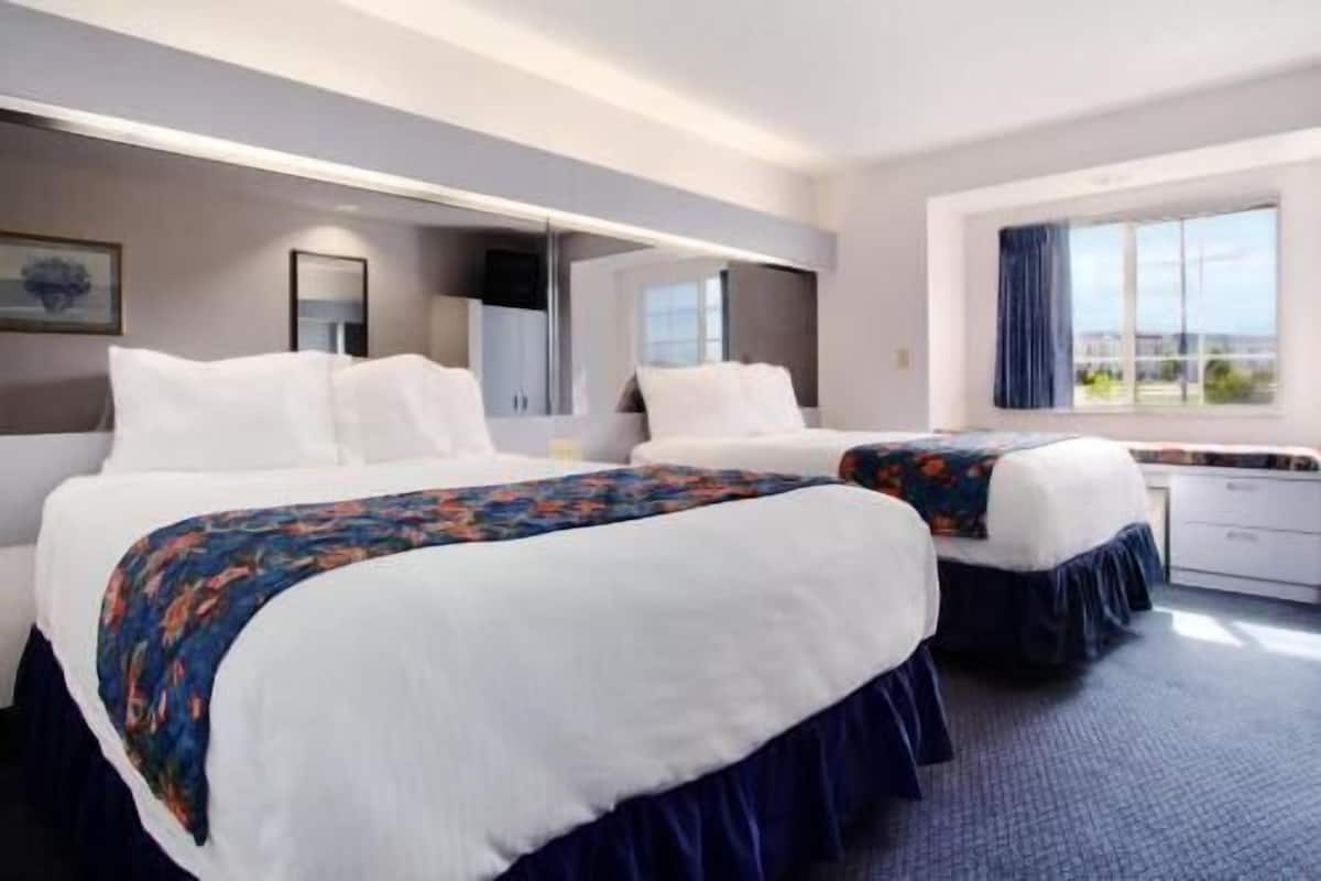 Habitación de hotel con dos camas, un escritorio y ventana con vistas.