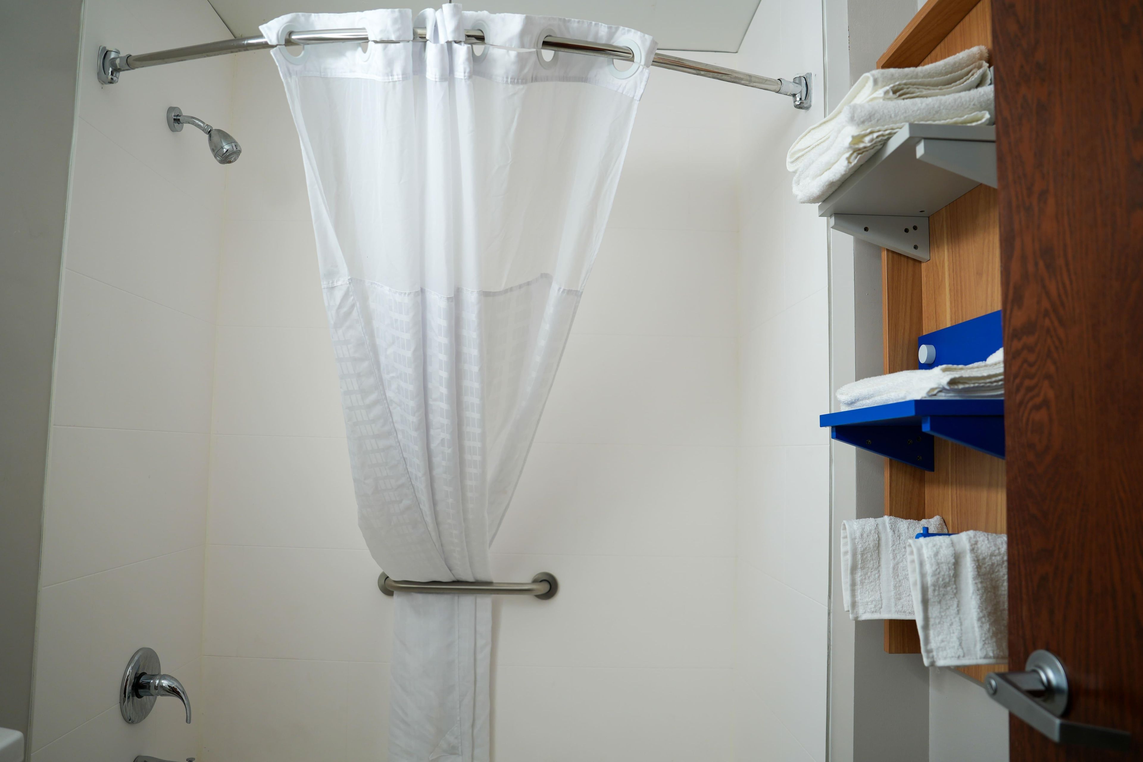 Une douche avec un rideau blanc, un porte-serviettes avec des serviettes et une porte en bois.