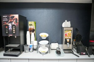 Una estación de café con máquina de Nescafé, plancha para gofres y varias tazas y cuencos.