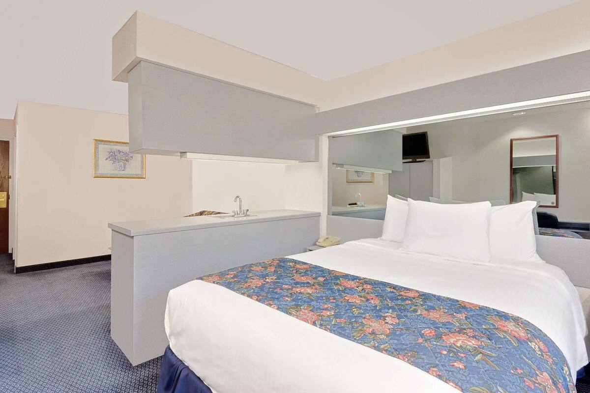 Habitación de hotel con cama, escritorio, espejo y televisión.