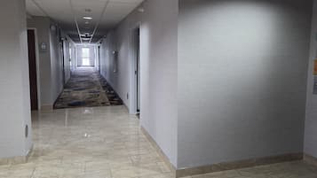 A hotel corridor with a patterned carpet, tiled floor, and doors leading to rooms.