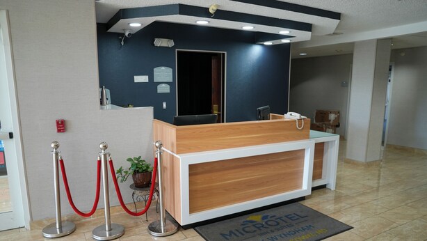 A reception desk with a wooden finish, a red velvet rope barrier, and a fire alarm sign on the wall. - Microtel Inn & Suites by Wyndham Hagerstown by I-81 (Hagerstown)