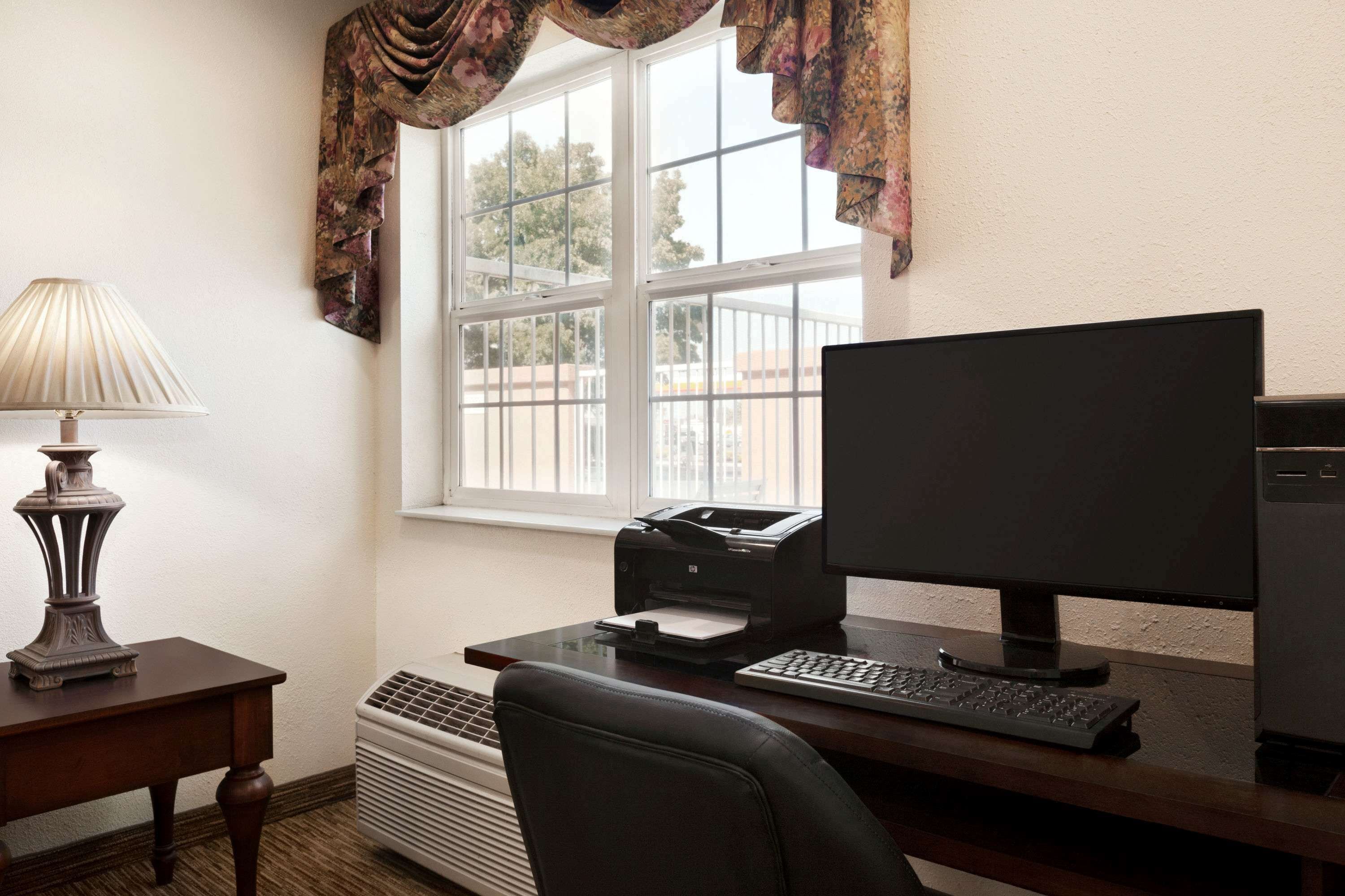 A home office with a desk, computer, printer, lamp, and air conditioner.