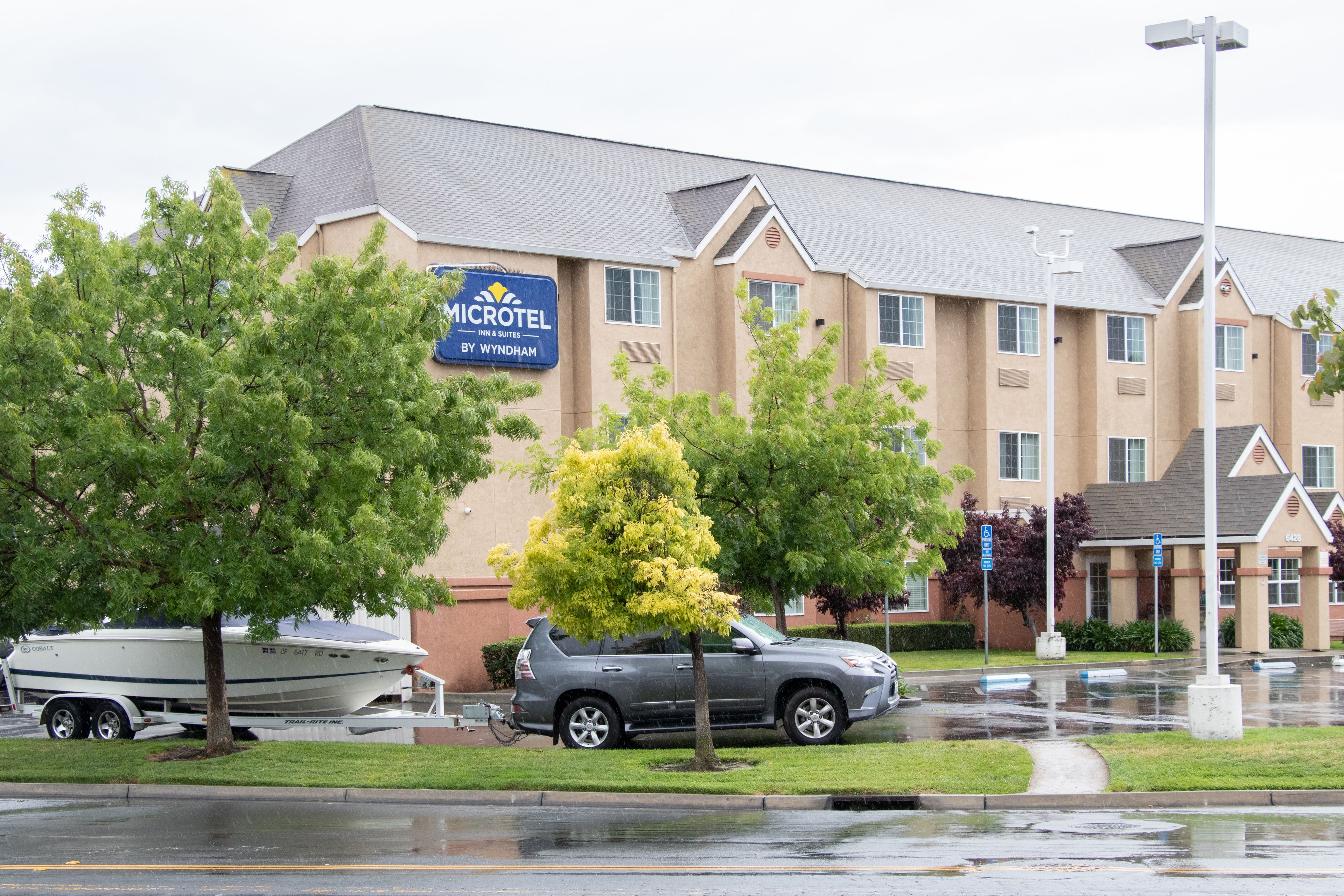 A Microtel Inn & Suites building with a boat trailer and a gray SUV parked in front.