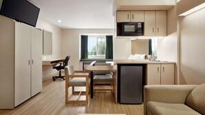 A compact hotel room with a kitchenette, a dining area, a sofa, and a TV mounted on the wall. - Microtel Inn & Suites by Wyndham Lodi/North Stockton (Lodi)