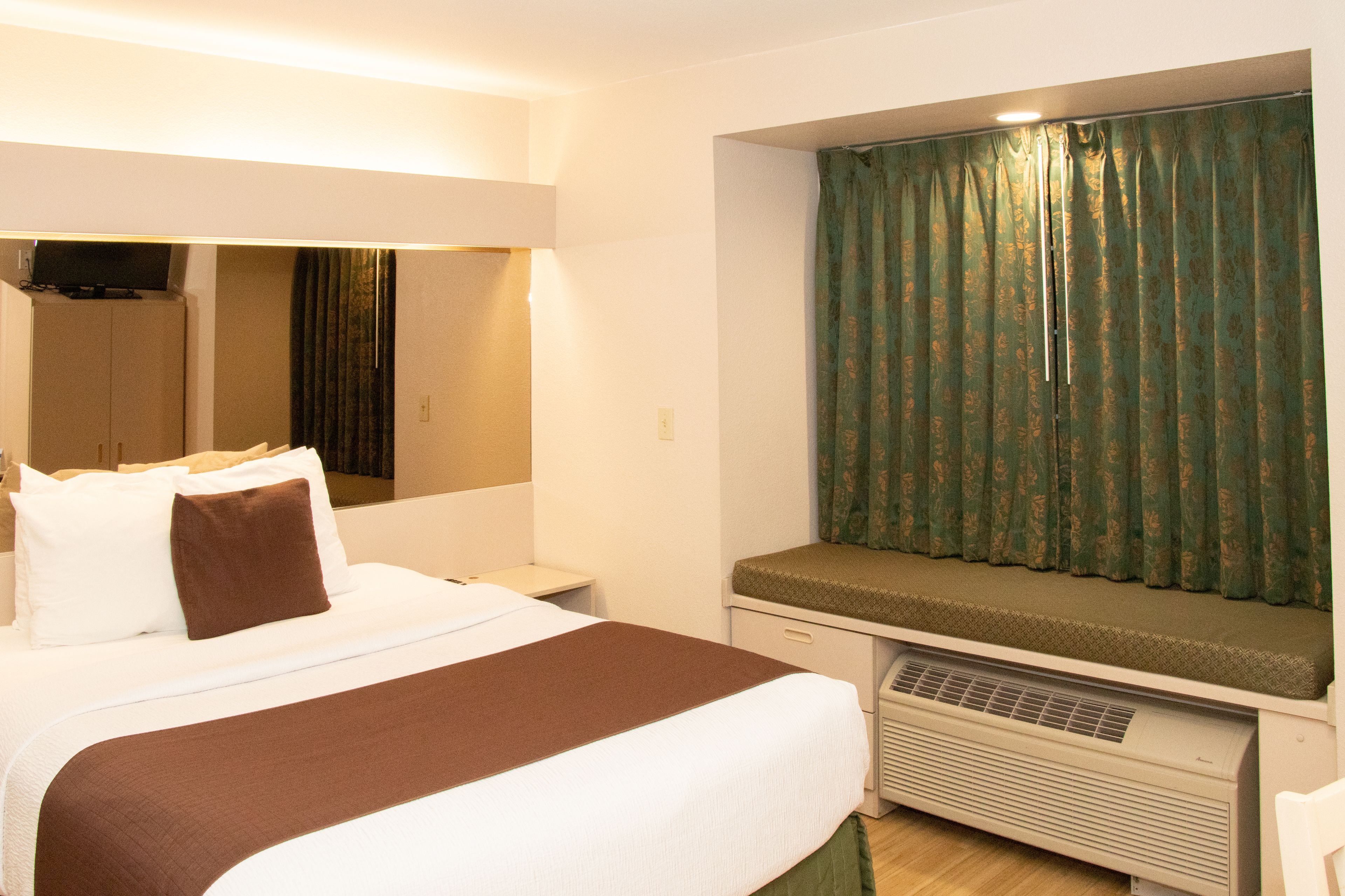 A hotel room with a large bed, a bench at the window, and a flat-screen TV on the wall.