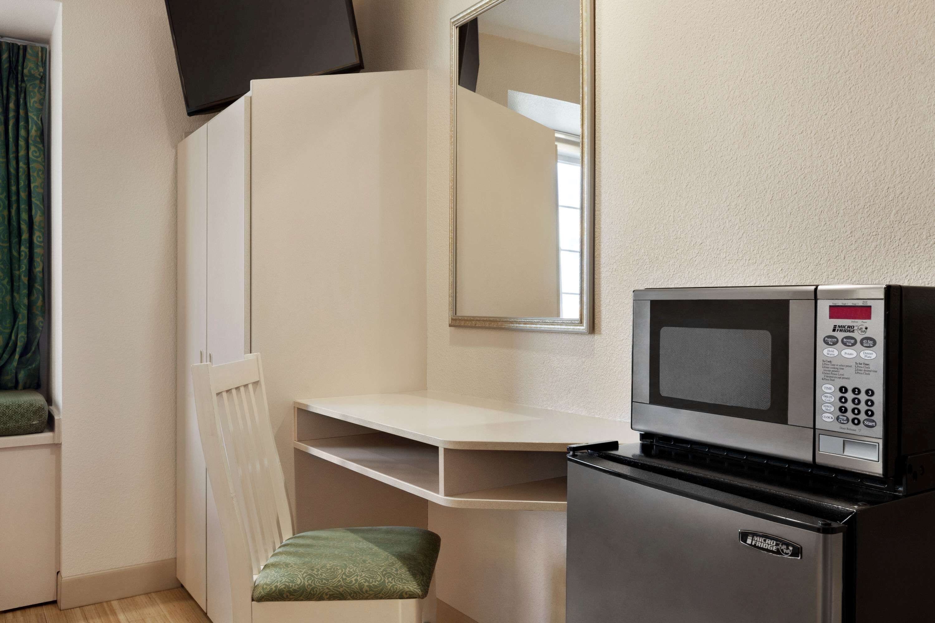 A compact kitchenette with a microwave, a small refrigerator, and a chair with a green cushion.