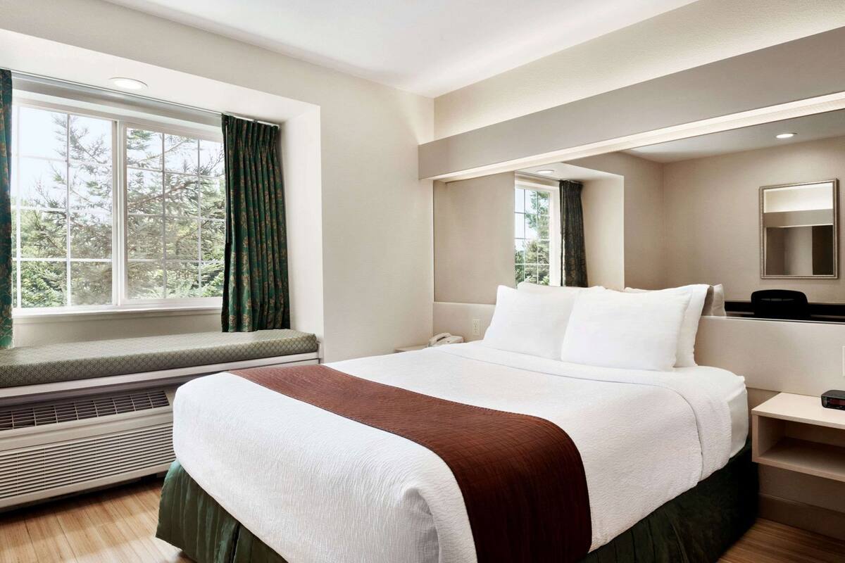A hotel room with a large bed, a window with curtains, a bedside table, and a heater.