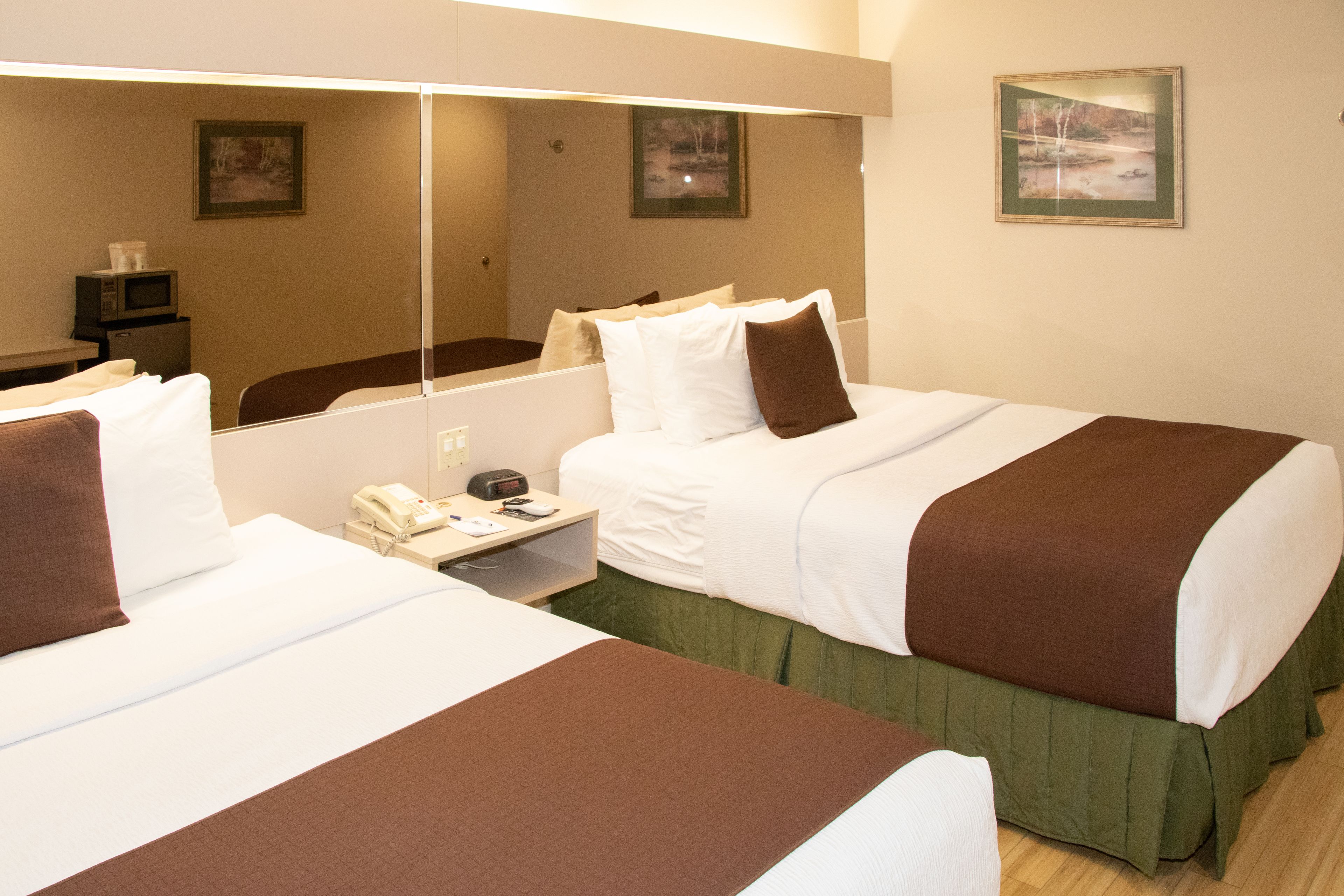 Habitación de hotel con dos camas, una mesita de noche con teléfono y reloj, y un espejo que refleja la habitación.