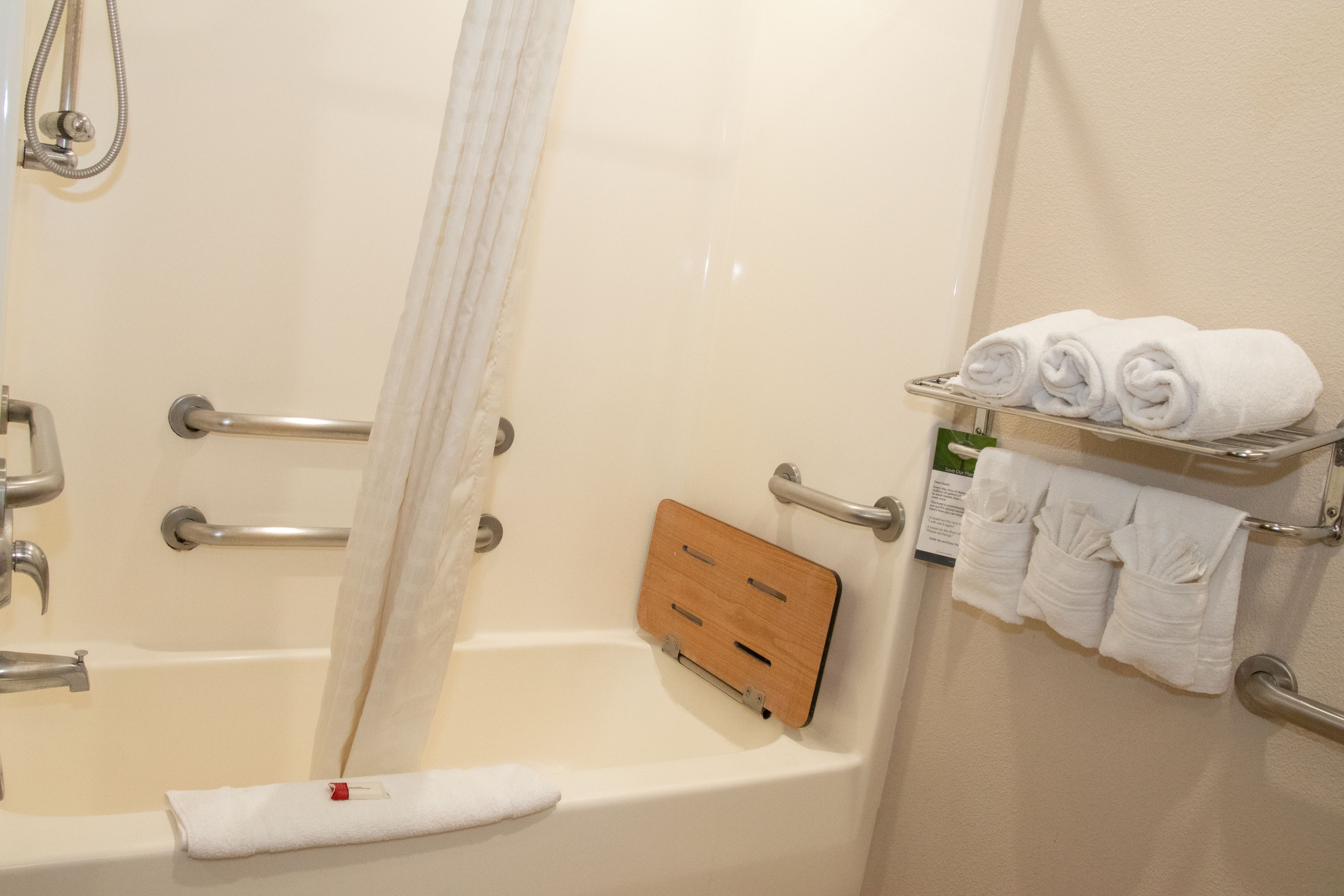 Una bañera con una bandeja de madera, un perchero con toallas enrolladas y un cabezal de ducha.