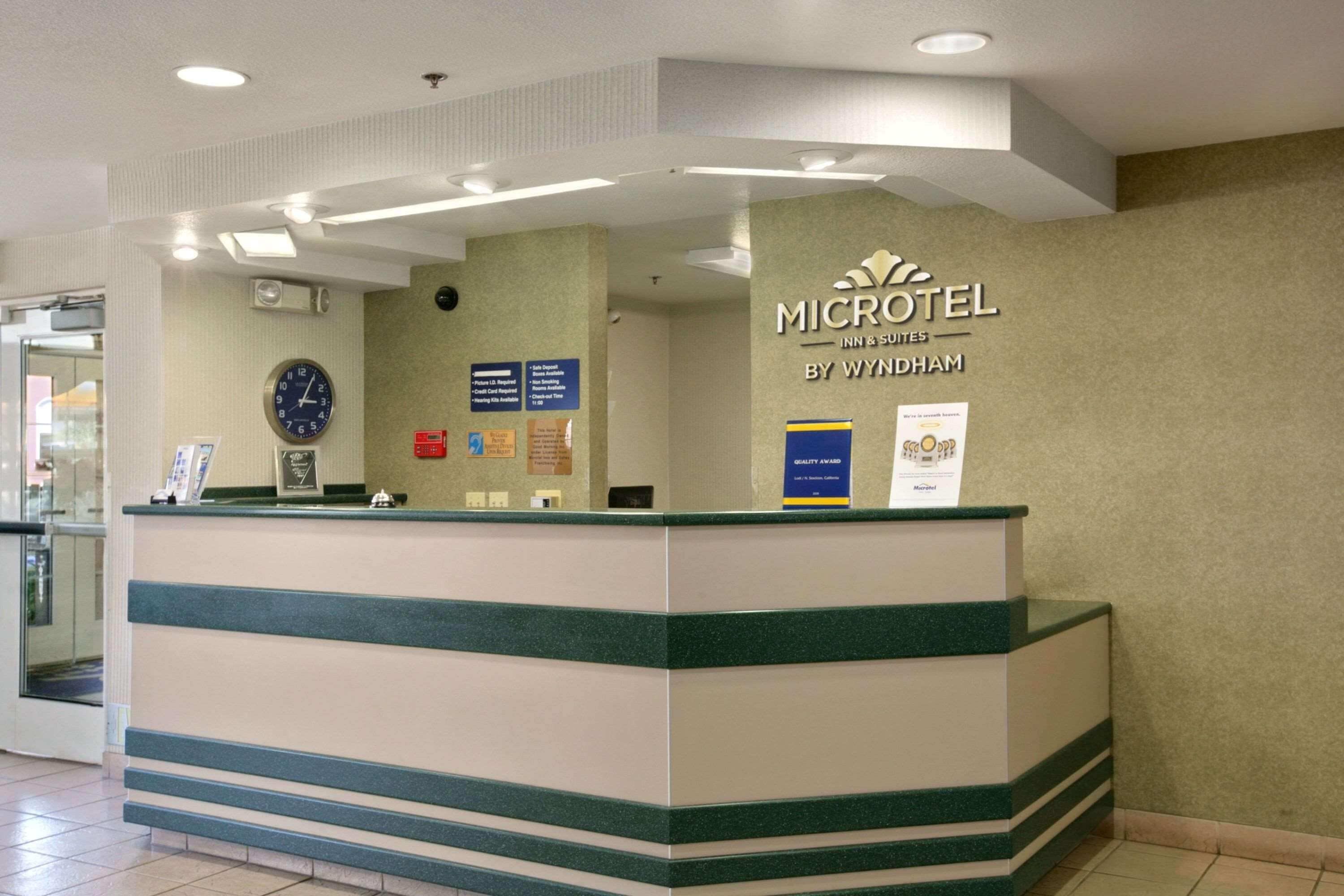 A reception desk with a clock, informational signs, and a sign for Wyndham Microtel Inn & Suites.