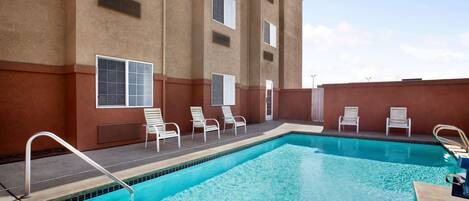 A swimming pool with white lounge chairs and a metal ladder.