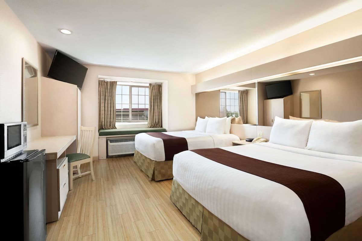 A hotel room with two beds, a desk, a TV, and a window with curtains.