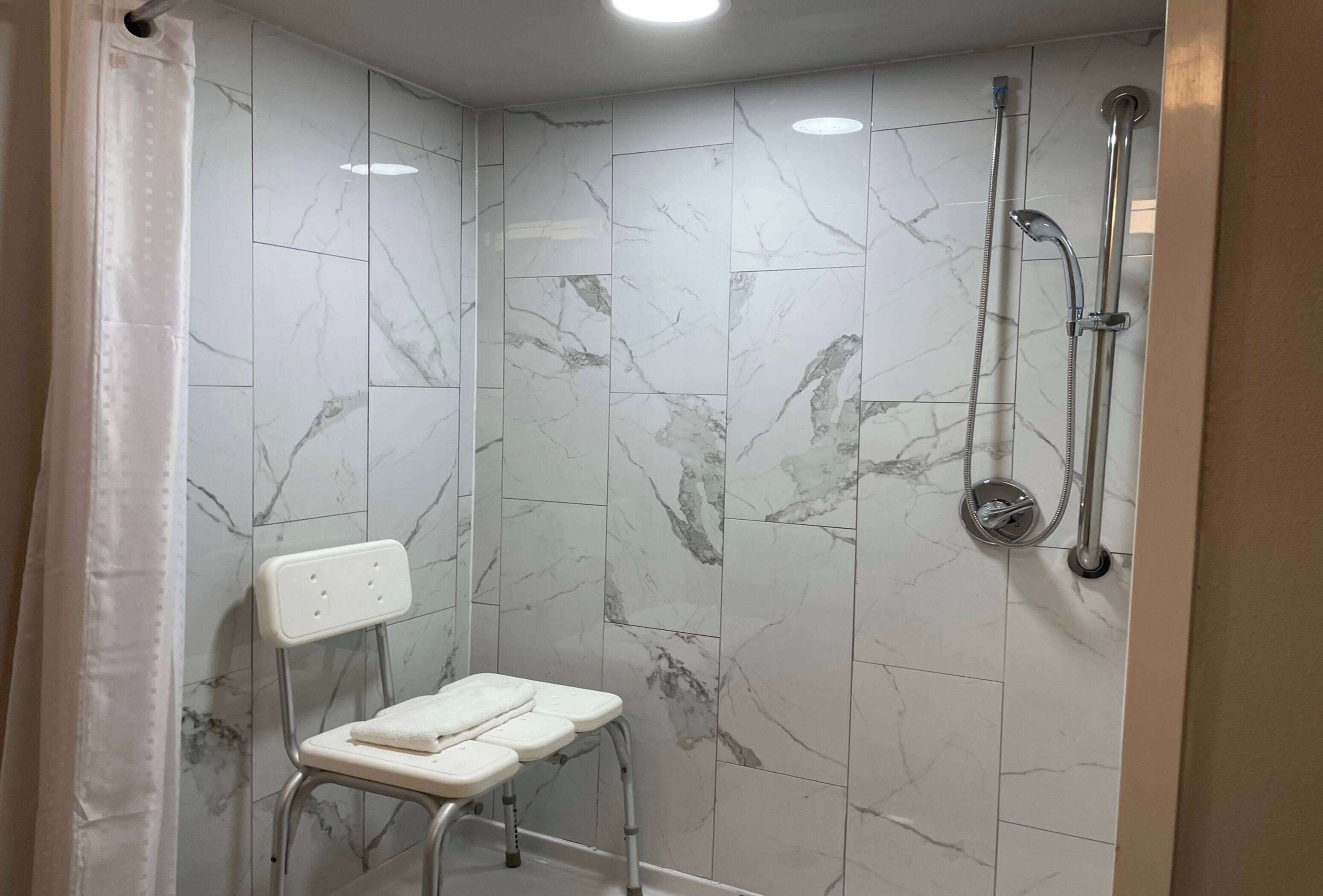 A bathroom with a shower, a white chair, and a tiled wall with a marble pattern.