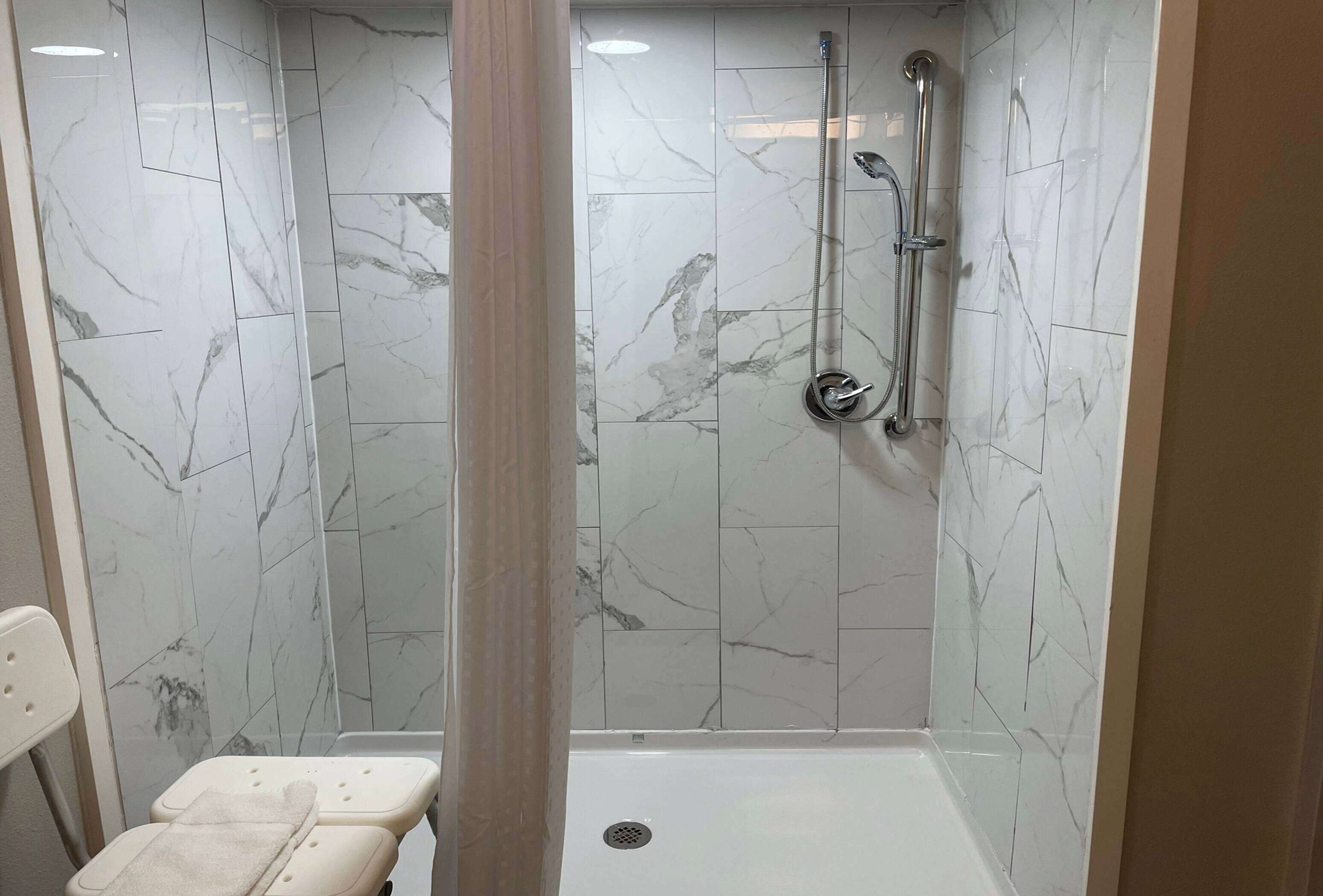 A walk-in shower with a glass door, marble tiles, and a handheld showerhead.