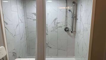 A walk-in shower with a glass door, marble tiles, and a handheld showerhead.