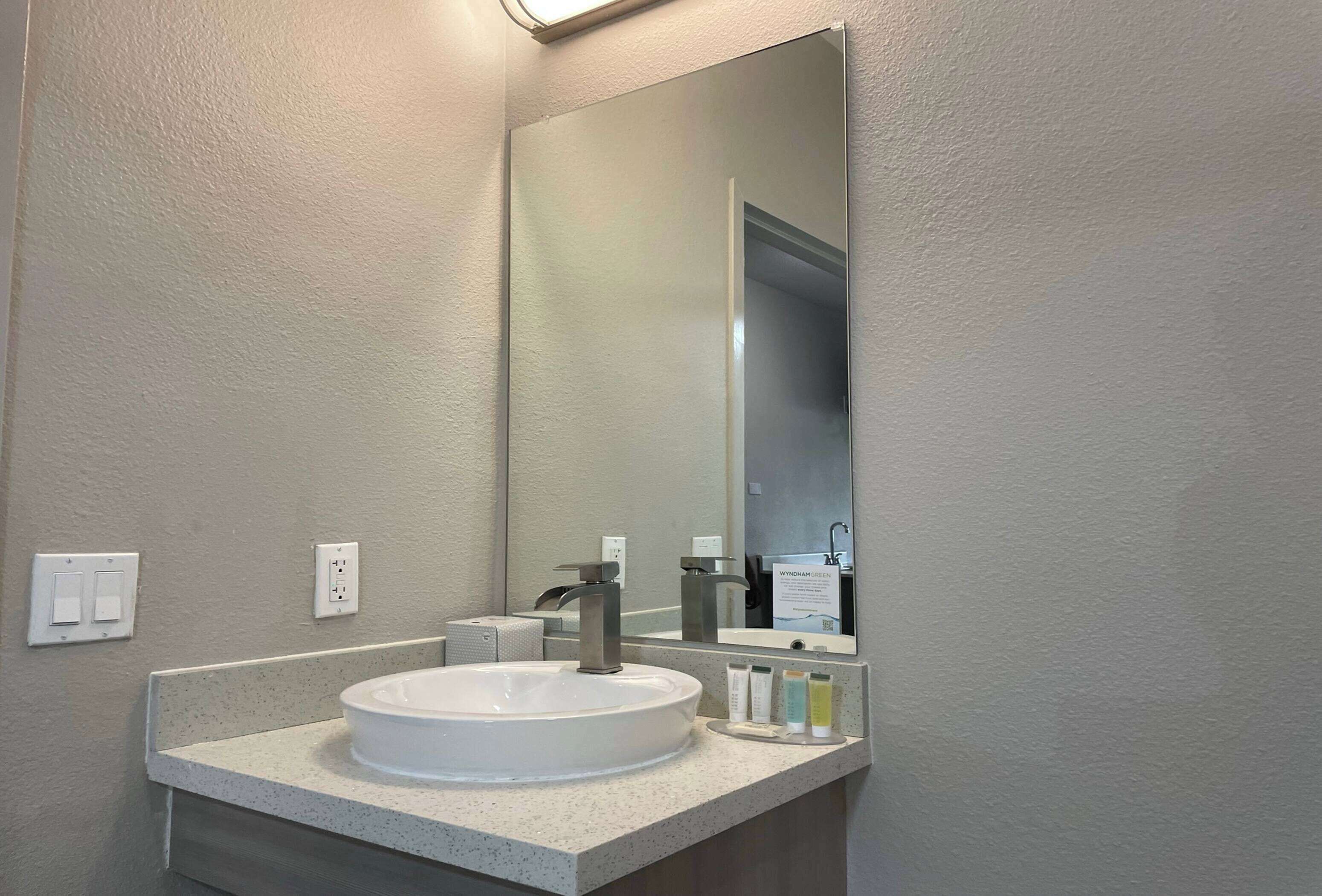 A bathroom with a white sink, a large mirror, and a countertop with toiletries.