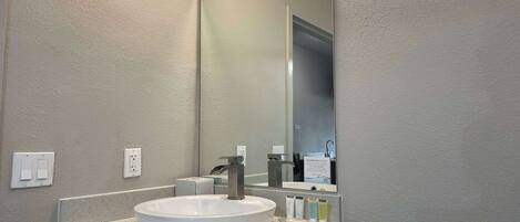 A bathroom with a white sink, a large mirror, and a countertop with toiletries.