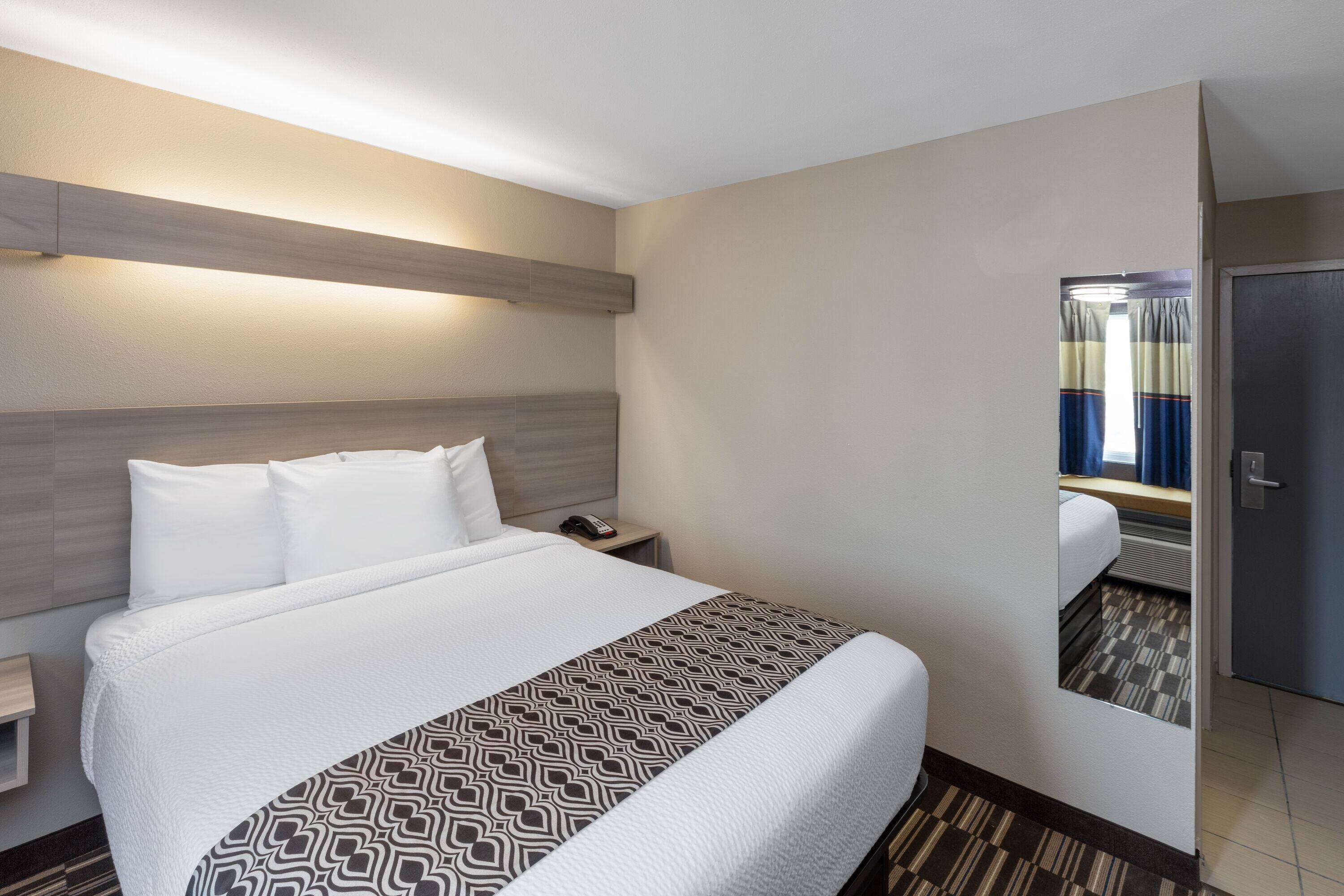 A hotel room with a large bed, a bedside table, a nightstand, and a door leading to another room.