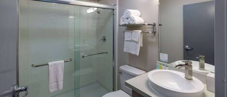 A modern bathroom with a glass-enclosed shower, a white toilet, and a sink with a mirror above it.