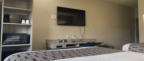 Habitación de hotel con cama, televisor montado en la pared, microondas y cafetera en un estante.