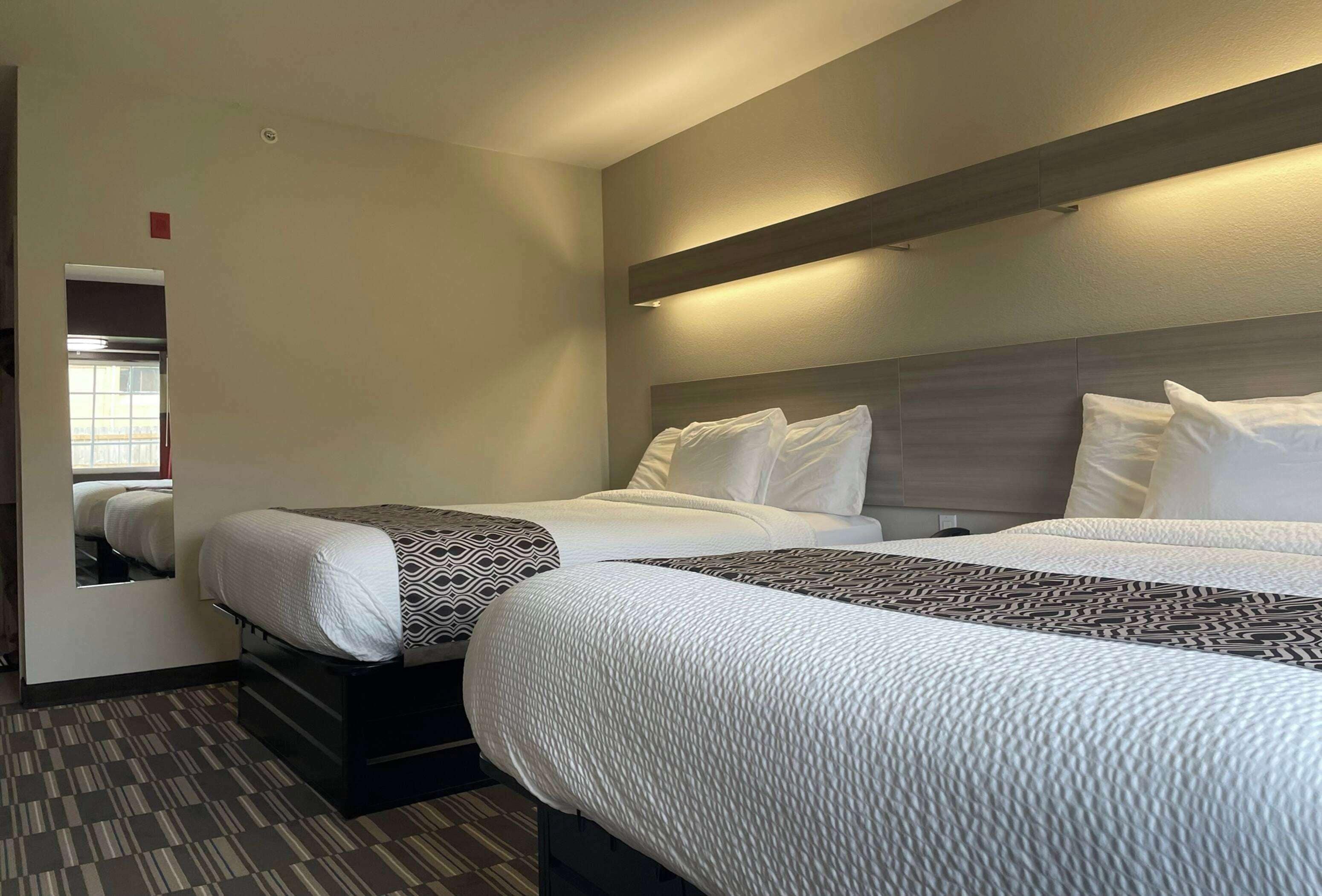 A hotel room with two beds, a large mirror, and a view of the city.