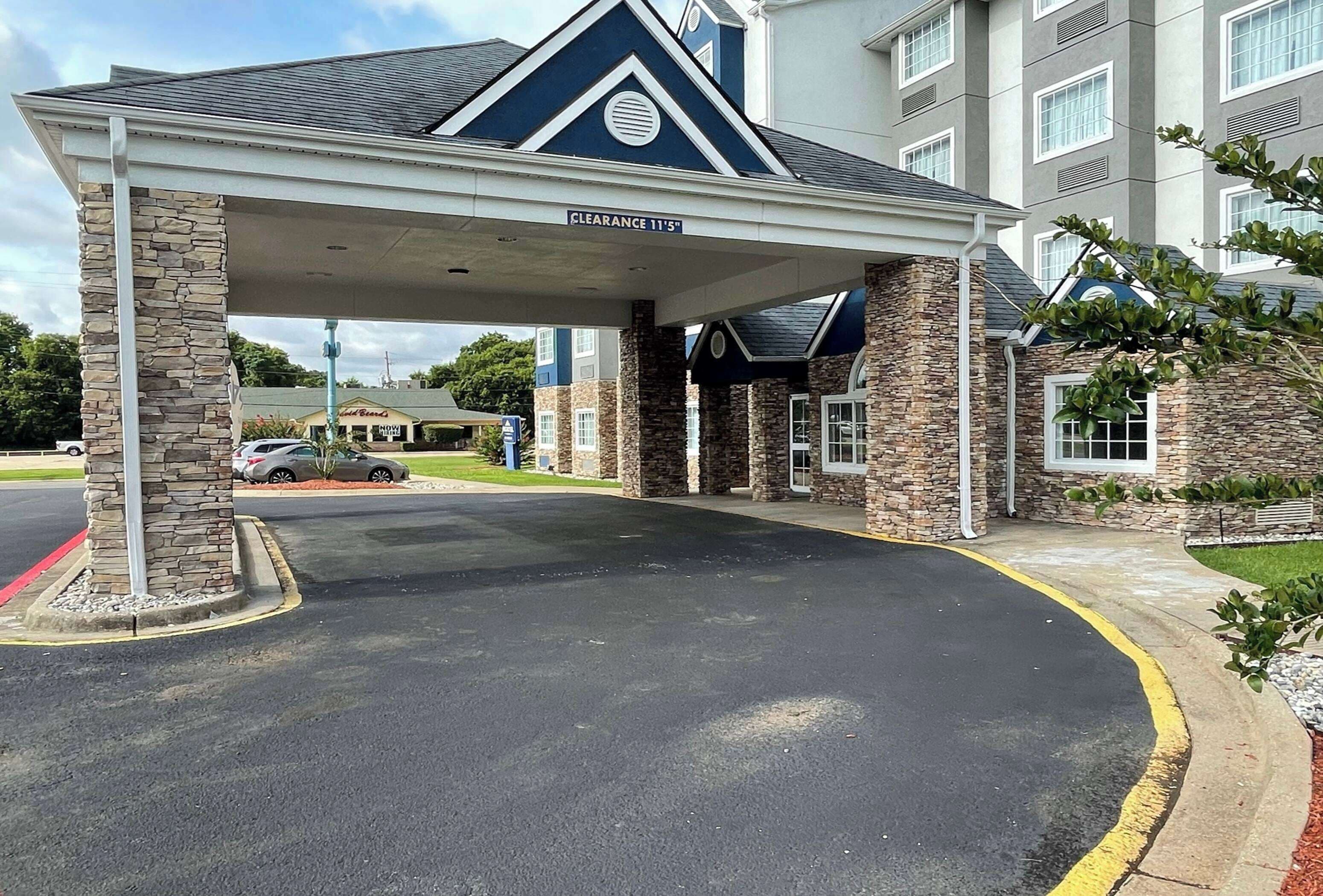 Entrada de hotel con zona de estacionamiento techada, pilares de piedra y un cartel que indica una altura máxima de 3.5 metros.
