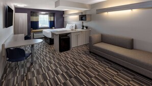 A hotel room with a bed, a sofa, a desk with a chair, a TV, and a microwave. - Microtel Inn & Suites by Wyndham Bossier City (Bossier City)