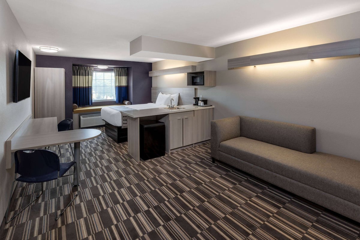 Une chambre d’hôtel équipée d’un lit, d’un canapé, d’un bureau avec une chaise, d’une télévision et d’un four à micro-ondes.