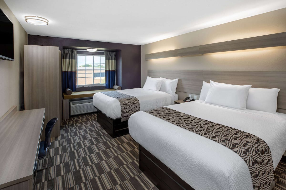 Une chambre d’hôtel avec deux lits, un bureau et une fenêtre avec des rideaux.