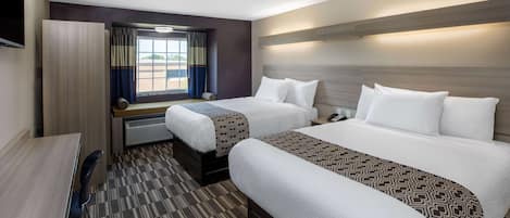 Una habitación de hotel con dos camas, un escritorio y un ventanal con cortinas.
