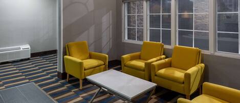 A room with yellow armchairs, a small table, and a large window with a view of the outside.