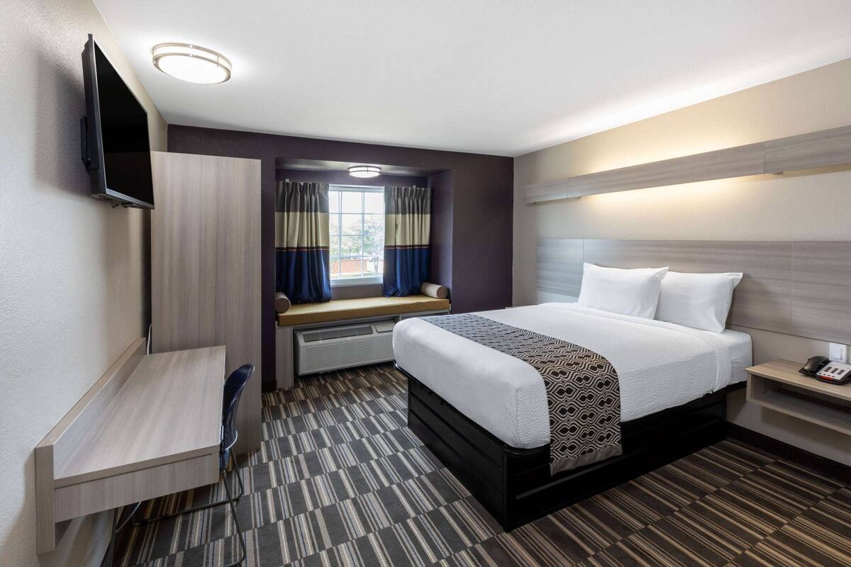 Une chambre d’hôtel équipée d’un lit, d’un bureau, d’une télévision, d’une fenêtre avec des rideaux et d’un radiateur.
