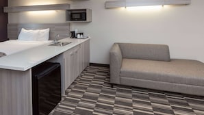 A hotel room with a bed, a sofa, a kitchenette, and a patterned floor. - Microtel Inn & Suites by Wyndham Bossier City (Bossier City)