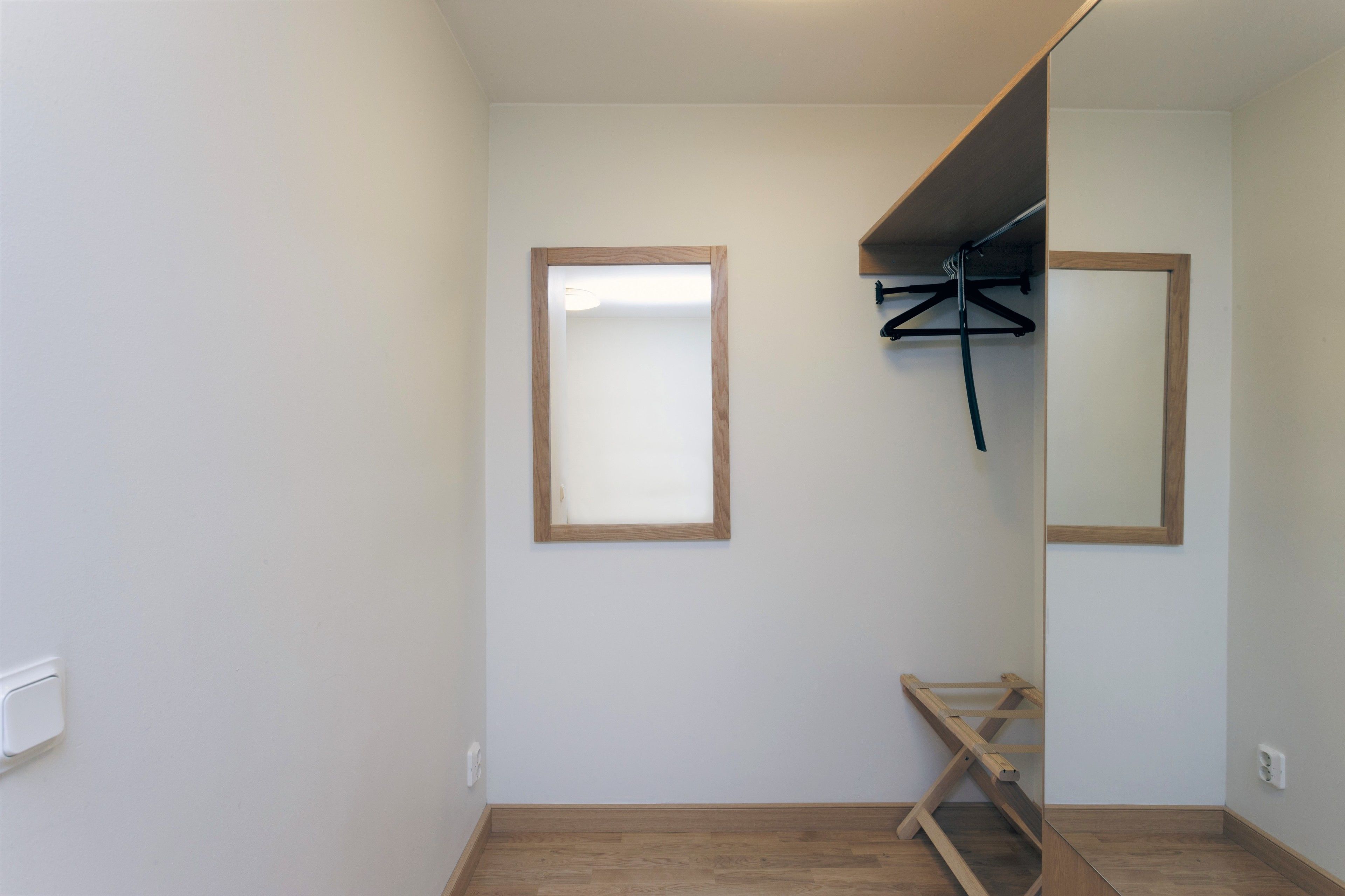 A small, clean room with a wooden floor, a mirror, and a wooden bench.
