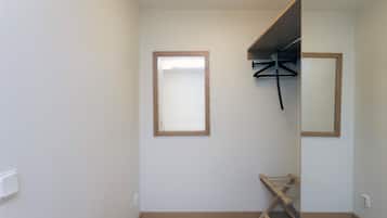 A small, clean room with a wooden floor, a mirror, and a wooden bench.