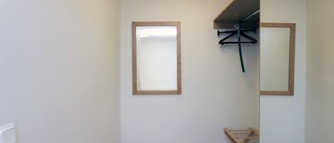 A small, clean room with a wooden floor, a mirror, and a wooden bench.