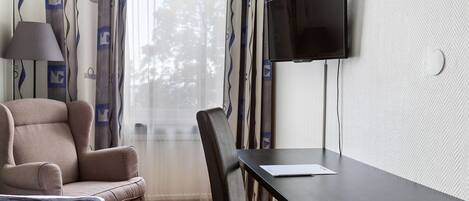 Habitación de hotel con cama, sofá, mesa de comedor, televisor montado en la pared y ventana con cortinas.