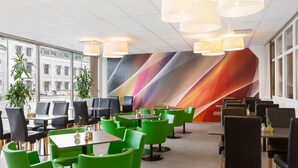A modern dining area with green and black chairs, tables, and a colorful wall mural.