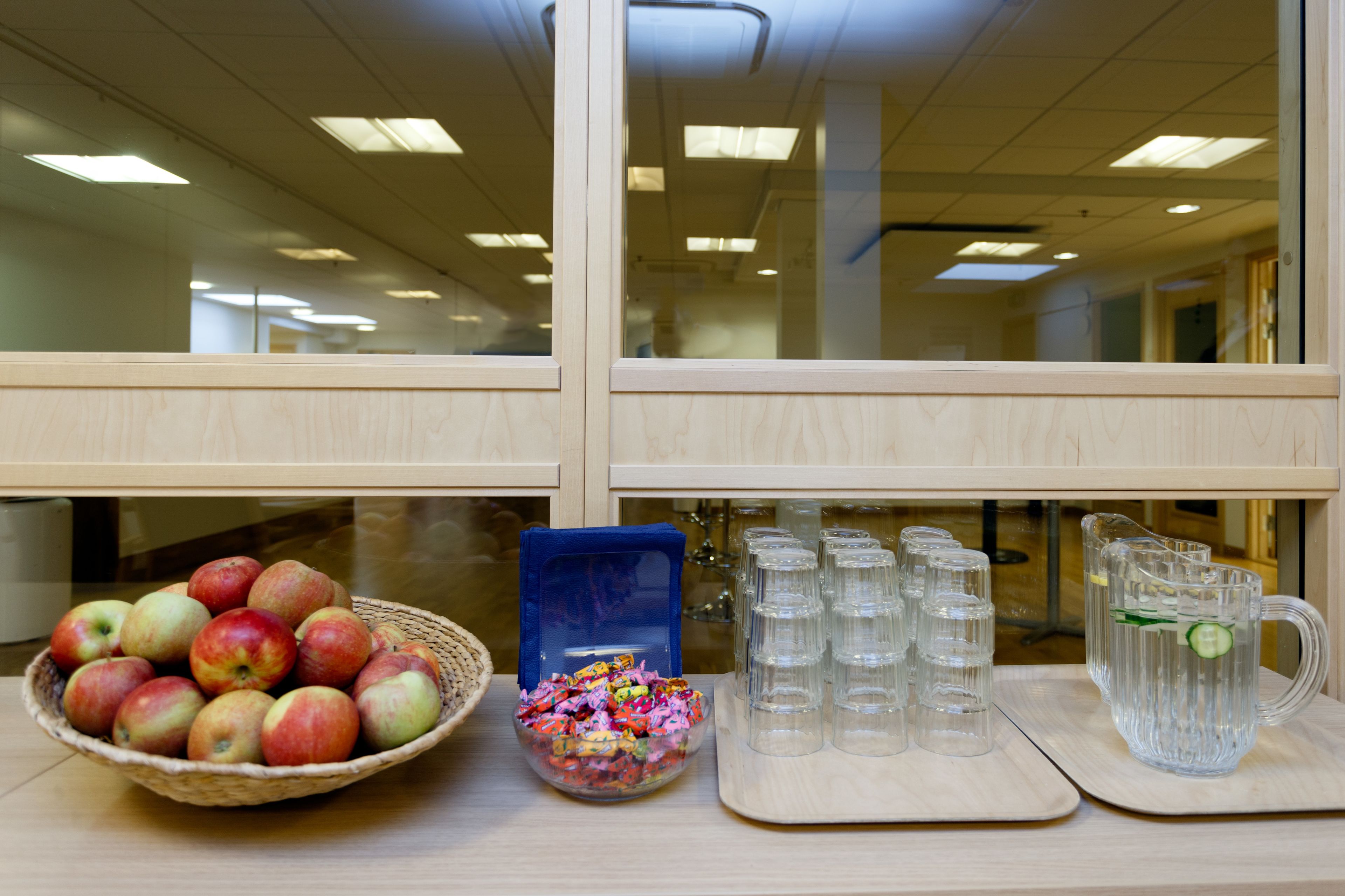 A desk with a basket of apples, a bowl of candy, and a pitcher of water.