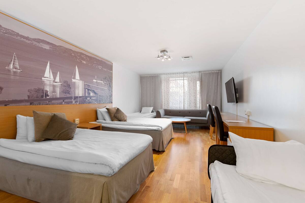 A hotel room with two single beds, a sofa, a desk, and a TV.