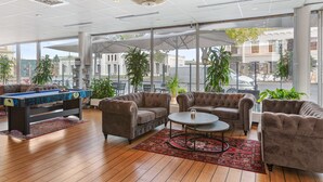 A spacious indoor area with a pool table, sofas, and a coffee table. Large windows offer views of the street and buildings outside.