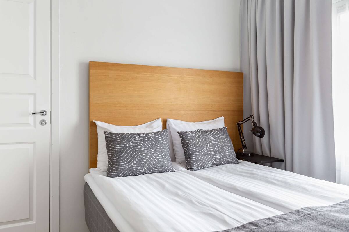 A neatly made bed with a wooden headboard, two patterned pillows, and a bedside lamp.