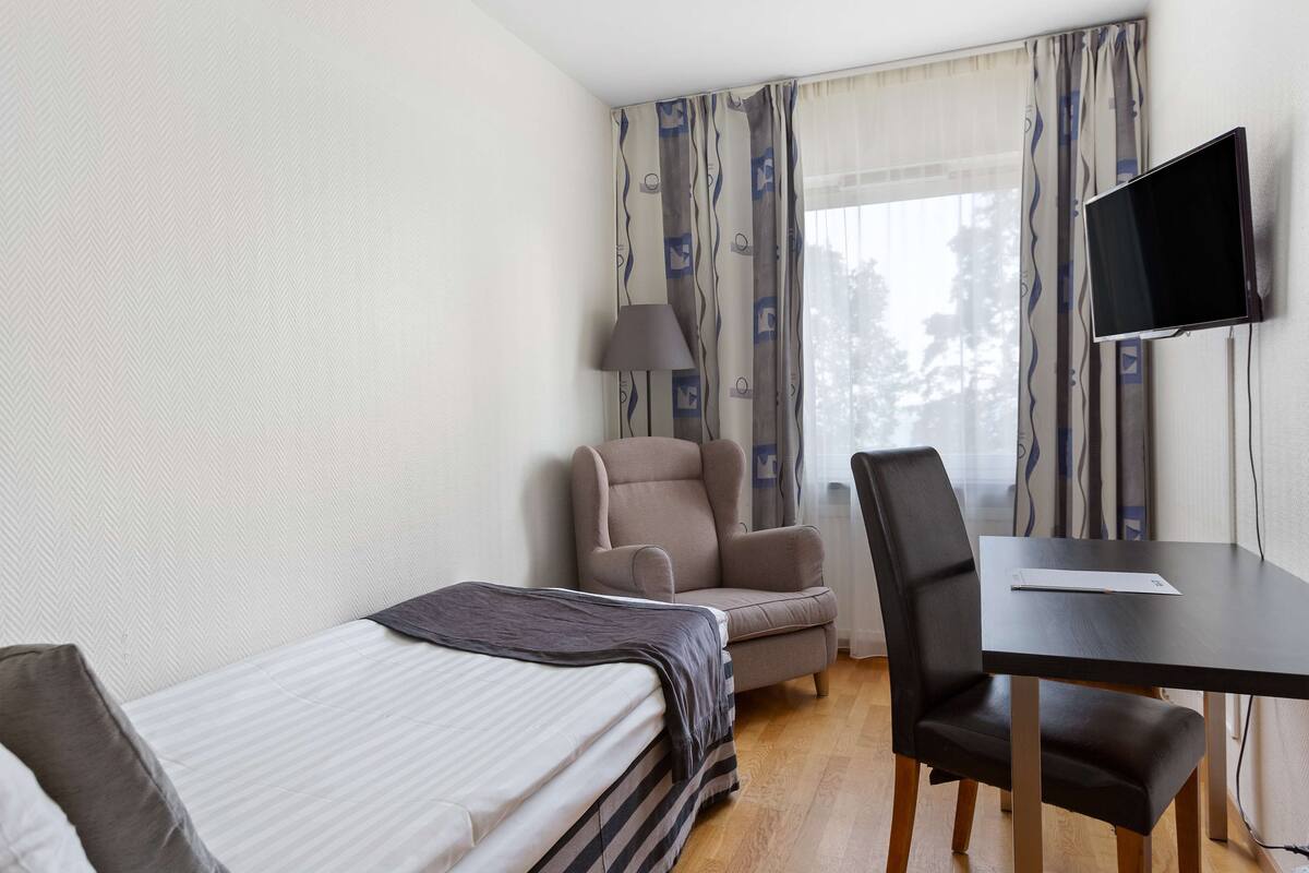 A hotel room with a bed, a desk, a chair, a television, and curtains.