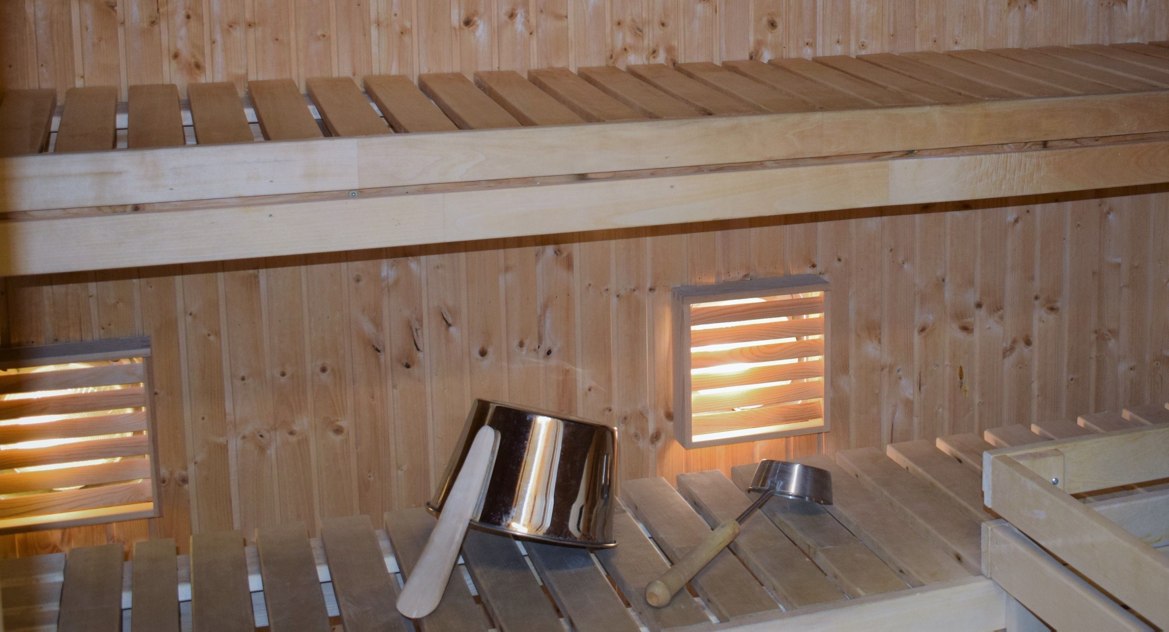 A wooden sauna with benches and a metal bucket.