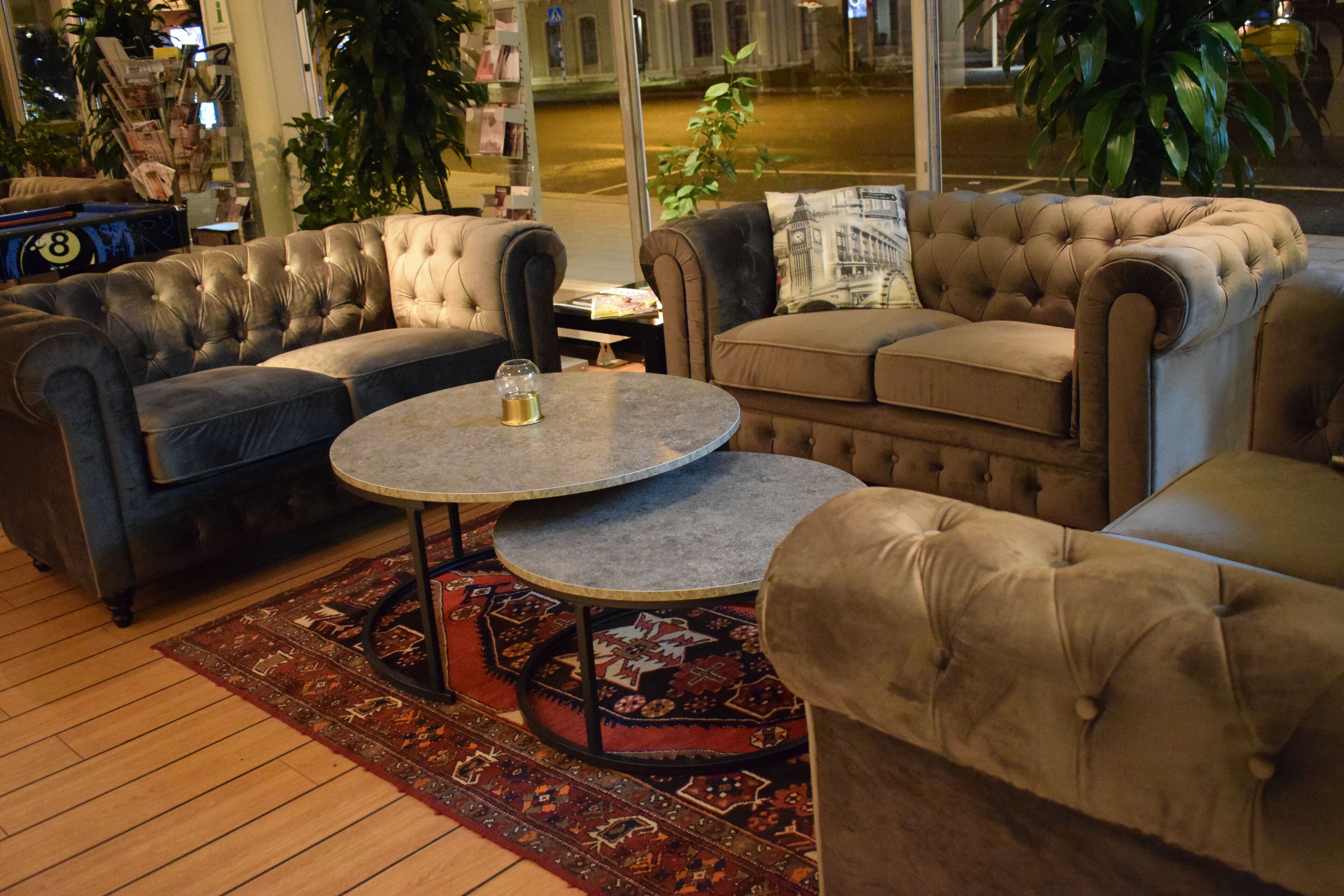 A cozy lounge area with plush sofas and a round coffee table, featuring a patterned rug and a view of the street outside.