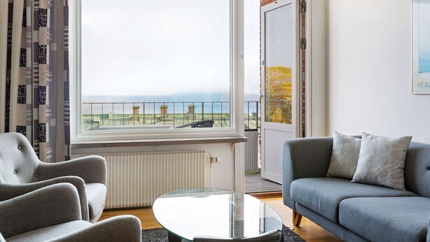 A living room with a grey sofa, a glass coffee table, and a view of a balcony with a railing.