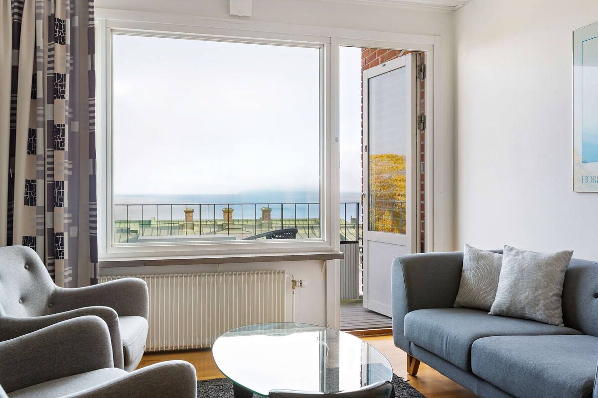 A living room with a grey sofa, a glass coffee table, and a view of a balcony with a railing.